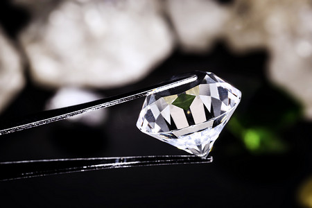 切割钻石由珠宝商的镊子持有，以毛坯钻石为背景，定点