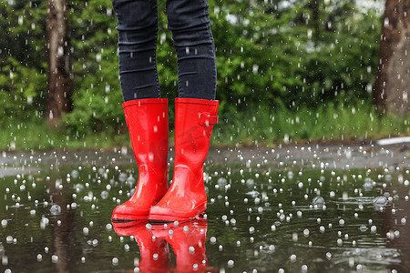 红色颐和园摄影照片_雨天站在户外穿着红色橡胶靴的女人带着冰雹和特写 