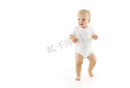 可爱的婴儿学会了在白色孤立的背景下走路。穿着白衣快乐微笑的孩子迈出了自信的第一步
