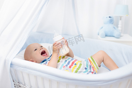 婴儿喝牛奶。床上有配方瓶子的男孩