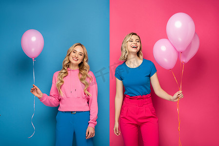 气球粉色摄影照片_快乐的金发女孩拿着蓝色和粉色背景的气球