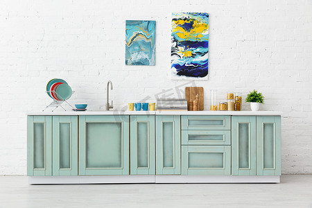 现代白色和绿松石厨房内部与厨房用具和抽象画在砖墙上