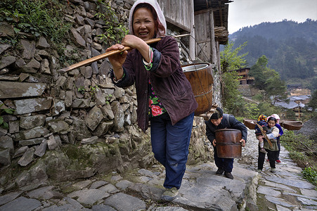 亚洲农民爬到山间小路行进，在肩膀上的负载.