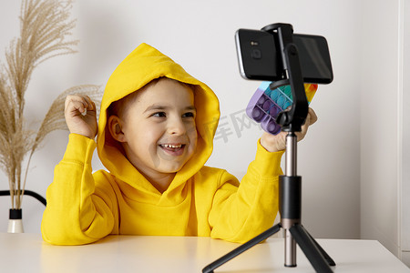 可爱可爱的小男孩博客记录生活方式博客，在三脚架上对着智能手机摄像机说话。年轻的影响者为他的频道拍摄vlog 。孩子在网上为他的追随者制作视频.