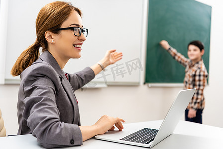 微笑的老师在眼镜与笔记本电脑指向用手在黑板