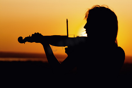 乐器表演摄影照片_日落时弹奏小提琴的女性人物形象简介、自然表演、下巴下夹着乐器的女孩、概念音乐艺术