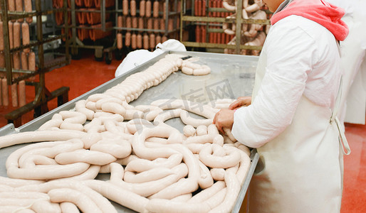 A worker prepares sausages on a table at a meat processing factory, food industry.