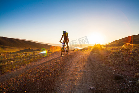 太陽升起摄影照片_女孩骑着自行车在冉冉升起的太阳的光芒