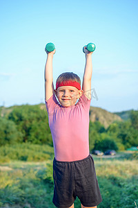 raising摄影照片_Smiling Strong Boy Raising Two Dumbbells