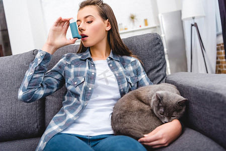 年轻女子使用吸入器, 而坐在沙发上与猫