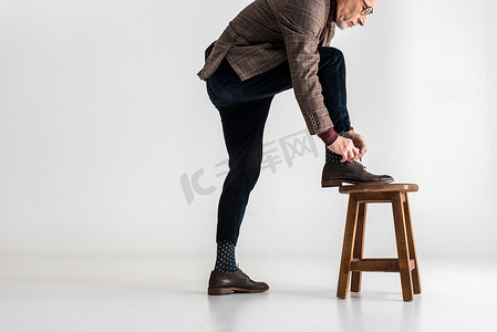 时尚成熟的男人把腿放在椅子上, 而绑在灰色的鞋带 