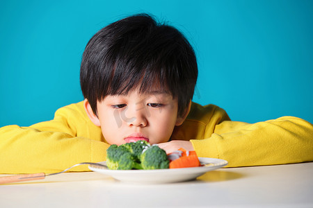 蓝色小学摄影照片_盯着蔬菜发愁的小男孩