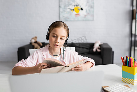 桌面上笔记本电脑旁耳机读物中儿童的选择性聚焦 