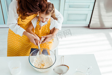 母亲和女儿在波尔卡点围裙的头顶视图混合面粉和鸡蛋与气球搅拌在碗