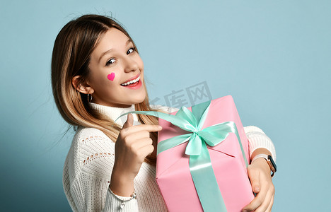 笑着的少女拿着一个大大的粉色礼品盒庆祝情人节，高兴地指着礼品盒