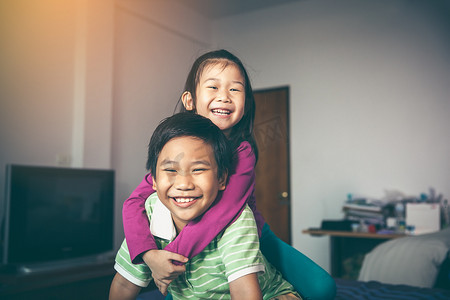 亚洲亲切的兄弟与他的妹妹背着骑和微笑高兴。可爱的孩子们在家里放松。兄弟姐妹概念的爱与结合。复古胶片过滤效果色调.