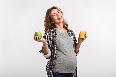 快乐怀孕的妇女拿着苹果和玻璃的果汁隔离在白色
