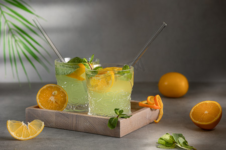 orange摄影照片_Glasses with lemonade or mojito cocktail with lemon orange and mint a cold refreshing drink on a gray background