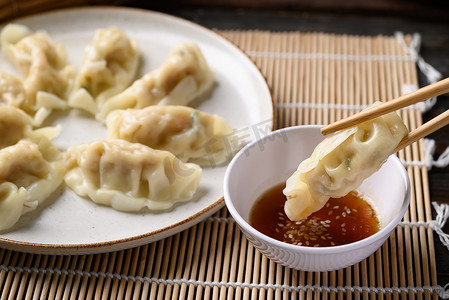 用筷子、亚洲菜和芝麻油酱汁在盘子里吃蒸笼饺子，里面塞满了碎猪肉和虾仁