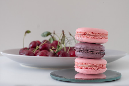 Close-up of appetizing mix of macarons on light background. Blurred plate with red cherries in background. Selective focus. Excellent image for dessert banners and advertisements. Place for your text.
