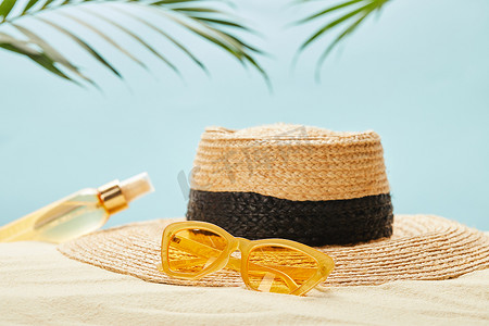 选择焦点黄色太阳镜接近草帽和瓶与防晒油在沙子查出在蓝色
