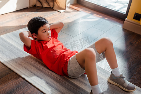 在检疫期间，亚洲男孩在家中健身垫上做腹肌运动