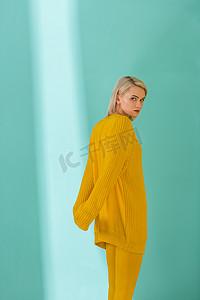 黄色毛衣和紧身衣的年轻女子侧面观看蓝色背景