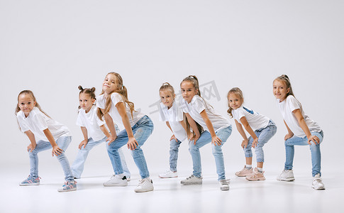 studio摄影照片_Joy, fun and happiness. Portrait of happy, active little girls, sportive kids in casual clothes dancing isolated on white studio background. Concept of music, fashion, art, childhood, hobby.