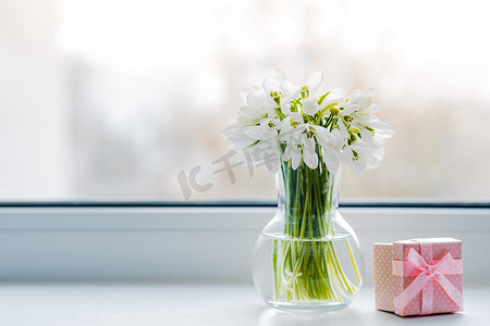 阳光雪花摄影照片_在春日的阳光下，美丽的玻璃雪花缀在窗台上，窗台上挂着一个粉色礼品盒。概念问候从三月八日母亲节，春天。自由空间，背景