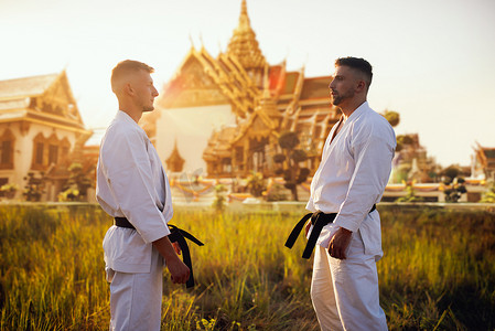 黑腰带空手道战士在白色和服上对古庙日落。户外武术训练。照片操作背景
