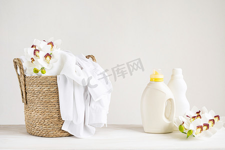 柳条篮，白色亚麻布，洗涤剂和织物柔软剂在白色桌子上，兰花。设有复印间的模拟洗衣店日.