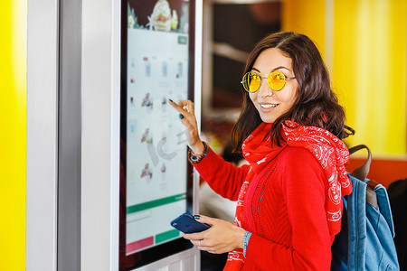 时髦的亚洲妇女在快餐餐厅的电子菜单上, 在触摸屏自助服务机上订购食物