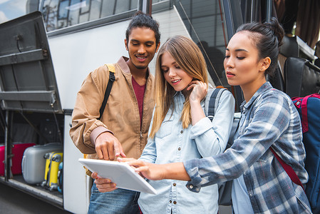 混合种族年轻人指着数字平板电脑的女性朋友附近的旅游巴士在城市街 