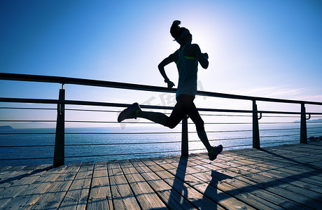 日出时跑在海滨木板路上的体态健壮的女跑步者