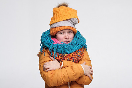 有趣的年轻的高加索女人，戴着几顶温暖的冬帽和围巾，在寒冷中发抖