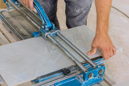 The construction worker cuts ceramic tile floor surfaces with manual tools and equipment in order to lay ceramic tiles on the floor.