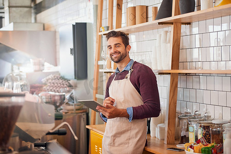 Coffee inspiration is never out of my reach. happy young business owner using a tablet while standing in his coffee shop