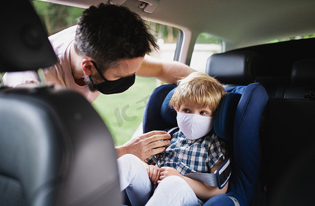 爸爸开车前把小儿子放在车座上，戴着口罩.