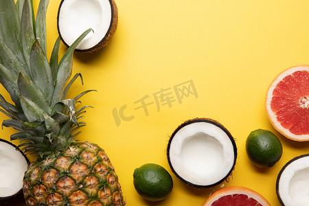 整个成熟的菠萝，柑橘类水果和椰子半黄色背景的顶视图