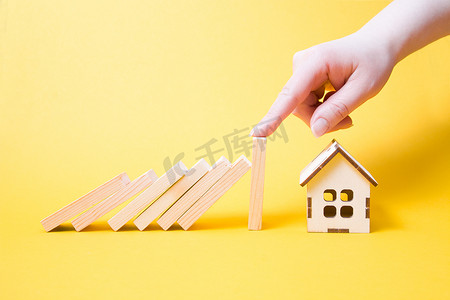 停止掉落木制多米诺骨牌掉落房屋模型，房地产保护概念，黄色背景，复制位置，财产保险概念