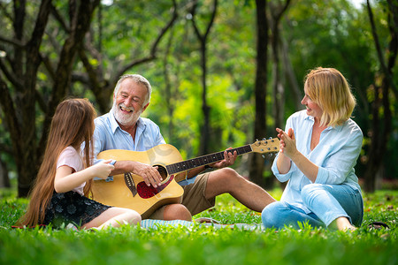 夏天, 快乐的家庭坐在公园里弹吉他, 一起唱歌。音乐中的家庭结合概念.