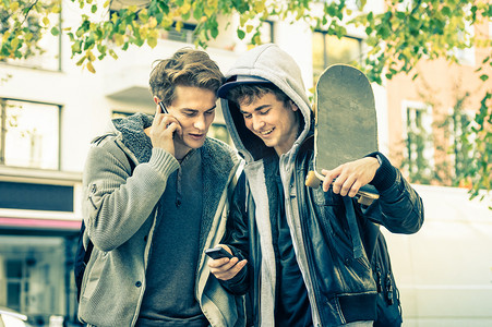 年轻时髦兄弟玩智能手机-最好的朋友分享自由时间与新趋势技术-享受日常生活时刻发短信的家伙与现代的智能手机设备连接
