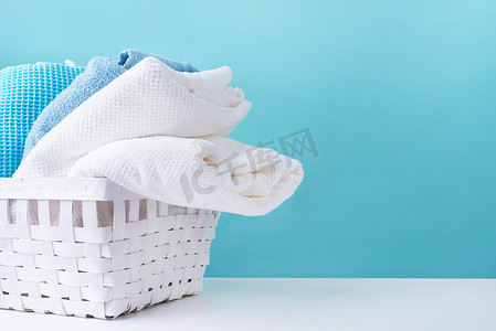 洗衣店的概念。一堆堆干净的毛巾放在蓝色背景的白色洗衣篮里