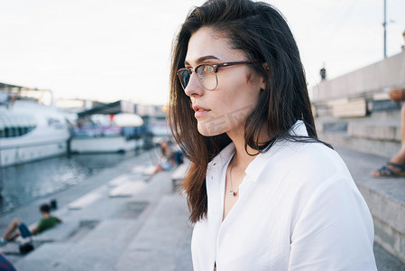 一张照片, 一个美丽的黑发妇女在眼镜穿着白色衬衫摆在城市公园背景