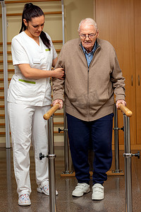 协助老年病人提供治疗棒的年轻女护士的全长肖像。老人做平行酒吧之间的康复.