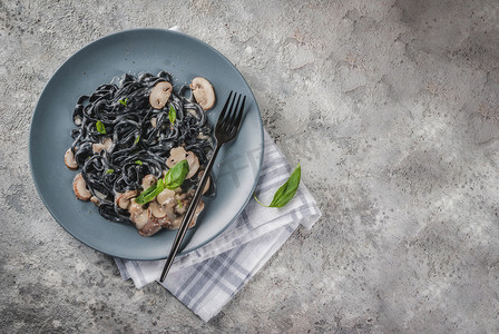 现代意大利晚餐, 地中海菜, 黑色墨鱼墨意大利面食与香菇蘑菇, 橄榄油和罗勒, 在灰色石桌上查看复制空间