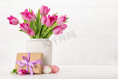 Fresh pink tulip flowers bouquet, easter eggs and gift box. On white wooden table with copy space