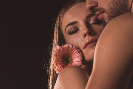 温柔的恋人闭着眼睛拥抱和持有非洲菊的花朵, 孤立在棕色 