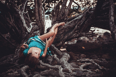 美丽的年轻女子，穿着绿松石躺在热带雨林中的树的根部。复古的颜色
