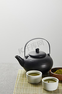 在红茶壶附近的木碗中选择性聚焦绿色火柴粉，在竹桌垫上加茶杯